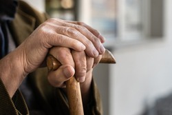 Close up on hands of unknown old caucasian man pensioner senior holding cane walking stick while sitting and waiting - real people old age senility concept copy space