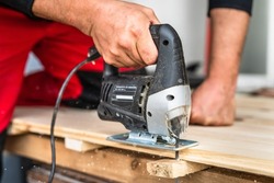 Close up on hand of unknown carpenter working with an electric jigsaw cutting wood with saw woodworking hobby concept