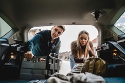 Two people couple students travel concept man and woman taking luggage baggage suitcase and other stuff and belongings from the back of car while moving into dormitory on college campus real people
