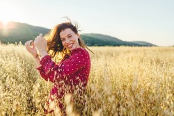 Portrait of adult caucasian brunette woman wearing red dress in summer day standing in the crops grain field smiling happy looking to the camera with copy space