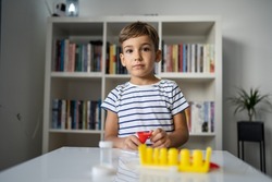One preschool boy playing at home sitting at the table with science experiments looking straight at the camera with serious face childhood growing up concept copy space front view