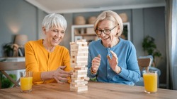 two senior women female woman friends or family sisters play leisure board game at home have fun pensioner grandmother spend time together with their mature daughter