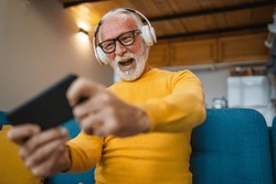 One senior old caucasian man sit at home happy smile play video games leisure activity having fun hold mobile phone smartphone have fun copy space