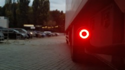 Close-up shot of the rear round red marker light of a truck. Rear light for a truck. The background is blurred. The concept of safe travel on the road at night.