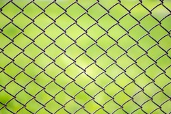Mesh cage in the garden with green grass as background. Metal fence with wire mesh. Blurred view of the countryside through a steel iron mesh metal fence on green grass. Abstract background