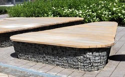 Wooden benches from gabion baskets with stones inside. Wood mounted on gabions. Benches of modern design. There is a recreation area. Detail of a low gabion wall with a wooden top