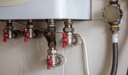 Hidden water taps for connecting a gas boiler on a tiled wall. Plumbing connections for a domestic double-circuit gas boiler. Pipes of the heating system. Installing a gas boiler with red taps