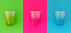 Arranged empty transparent  multi colored drinking glasses on colorful background minimalist copy space