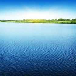 Blue sky with sun over water.
