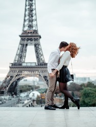 A young couple (a guy and a red-haired girl) of elite College students in white shirts embrace against the backdrop of the Eiffel tower in Paris. Student trip to Europe.