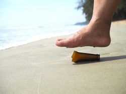 bare feet stepping on a broken brown glass bottle with a sharp tip on the beach concept danger of broken glass bottle on the beach