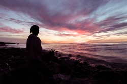 Silhouette of young woman wearing exercise clothes practicing yoga on the beach at sunset or sunrise. women do yoga. women exercising yoga in the beach.Young girl meditating in lotus posture.