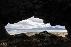 Outlines of an island inside the rock on Atlantic Ocean coastline, shore, where Basalt rock Hvitserkur is located, Iceland. View of the ocean and mountains through the hole in the rock. Island shape.