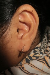Asian woman's ear on the left. Earrings in the ear                               