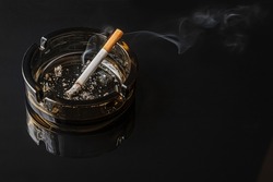 lit cigarette in a brown glass ashtray on a black mirror surface