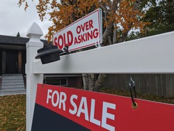 Fresh new sign sold over asking for sale in front of detached house in residential area. Real estate bubble, crash, hot housing market, overpriced property, buyer activity concept. Selective focus.