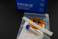 Covid-19 at home specimen collection rapid test kit box with sealed nasal swab and a sample transport tube with liquid placed on top of the bio hazard plastic bag.  Travel rules changes concept.