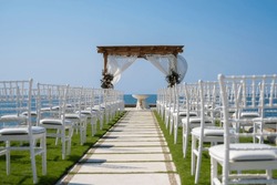 Wedding altar and row of white chairs shot at low angle prepared on the beach against a background of beautiful sea and blue sky. Destination wedding and celebration in a tropical country concept.