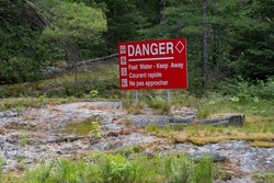 Bright red sign in the forest by the river in French and English danger fast water - keep away. Water safety concept.