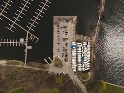 An aerial view above a large boat harbor, seen during the offseason with any empty water harbor and boats seen on land storage.