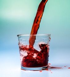 A glass beaker filled with a stream of red cherry juice. Color white and turquoise background. High contrast. Saturated color.