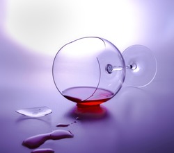 Fallen broken glass with the remnants of red wine in it. White purple background. Shard and drops. Elegant style.