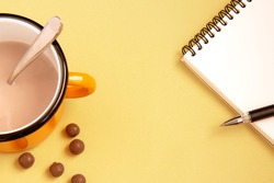Open white notebook with pen and iron orange cup with cocoa and chocolate balls on a delicate background. Flat lay. Selective focus