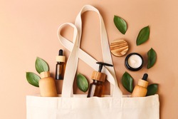 Open eco friendly cotton reusable bag with the different containers from the natural wood and brown glass.Fresh natural leafs around.Concept of organic,zero waste cosmetics.Woman bag with ac?essories.