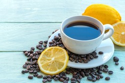 Lemon black coffee in white cup, coffee beans, lemon slices on soft green wooden background.