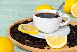 Black coffee in white cup and yellow lemon, lemon slices, on a wooden saucer, and on soft green old wooden background.