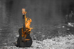 
black and white image, the main object is painted in orange. wooden guitar burns, outdoors, near the river