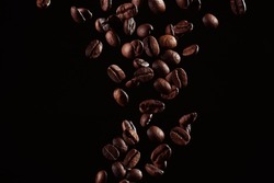 Roasted coffee beans falling against dark backdrop