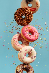 Various decorated doughnuts in motion falling on blue background. Sweet and colourful doughnuts falling or flying in motion.