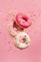 Various decorated doughnuts in motion falling on pink background. Sweet and colourful doughnuts falling or flying in motion.