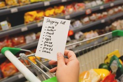 Woman with notebook in grocery store, closeup. Shopping list on paper. Check purchases in grocery cart.