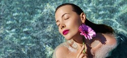 Beauty fashion portrait in water. Young beautiful  female model with make up and perfect skin posing with a pink daisy flower and swimming in the transparent sear or pool. Natural skin care concept