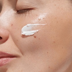 Cream smear. Beauty close up portrait of young woman with a healthy skin is applying a facial skincare product. Face  daily care routine 
