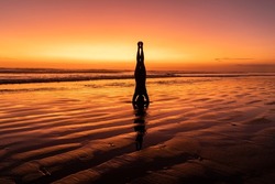 Girl meditating at sunset. Silhuette of young woman doing yoga at the beach. Headstand position 
