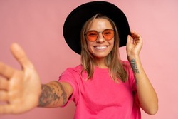 Close up studio photo of smiling young woman with tatoo on hands posing over pink background. 