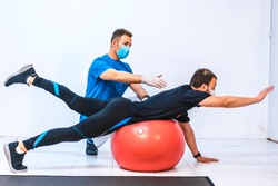 Physiotherapist with mask and a patient stretching on a ball. Physiotherapy with protective measures for the Coronavirus pandemic, COVID-19. Osteopathy, sports chiromassage