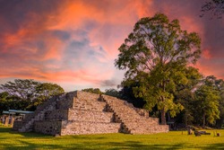 A Mayan pyramid next to a tree at the Copán Ruinas temples in a beautiful orange sunrise. Honduras