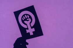 Shadow of the symbol of the fight for feminism on a purple background, clenched fist of a woman in the march protests for women's rights