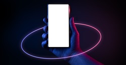 Phone in hand. Silhouette of male hand holding bezel-less smartphone with futuristic neon light circle on dark background. Screen is cut with clipping path.