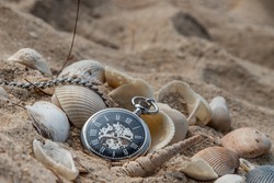 Antique pocket watch and shells in sand on the beach and copy space. Time of life in nature concept. Selective focus.