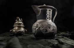 Chinese antique teapot (Characters chinese is Double Happiness) in frot of Silver antique incense burner on dark background. Chinese traditional style, Copy space, Selective focus.