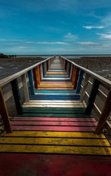 The walkway on Rainbow bridge or Old wood colorful bridge pier extends into the sea against blue sky and white clouds in afternoon at samut sakhon province. Selective focus.