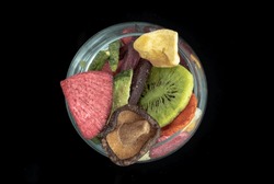 Different colorful dried fruits and vegetables in the glass with black background. Crispy mixed veggies and fruits, Healthy snacks food, Top view, Space for text, Selective focus.