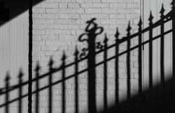 Wrought iron fence casts its stark shadow reflected on the adjacent white brick wall. Textured white brick wall with shadows of vintage fence, A wonderful background for your design. Selective focus.