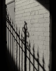 Wrought iron fence casts its stark shadow reflected on the adjacent white brick wall. Textured white brick wall with shadows of vintage fence, A wonderful background for your design. Selective focus.