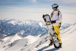 a male snowboarder in bright clothes stands against the background of the mountains. good weather. the sun is shining